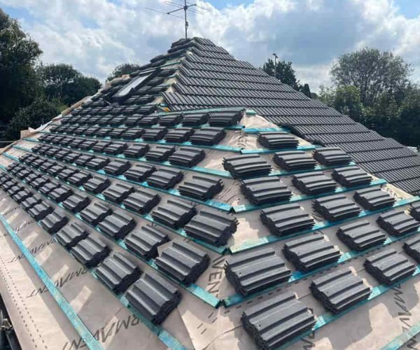 This is a photo of a new hip roof being installed. New felt, battens, and grey tiles have been installed, also a new velux window. Works carried out by DSC Roofing Rushden