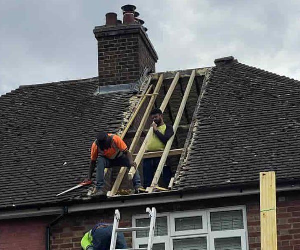 This is a photo of a roof repair being carried out. A section of the roof has been stripped and two roofers are replacing the rafters. Works being carried out by DSC Roofing Rushden